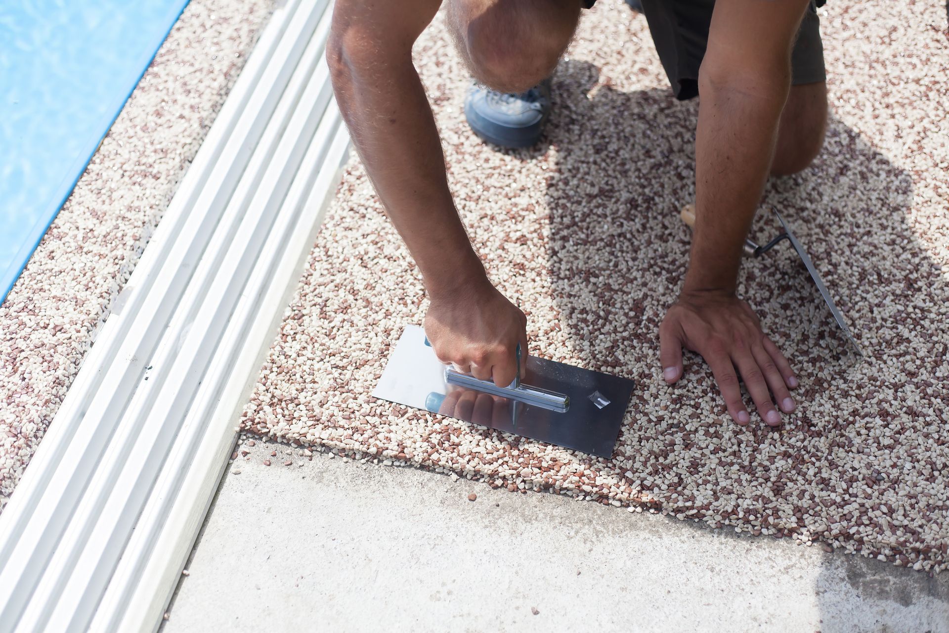 A man is kneeling down and using a trowel on a concrete surface.
