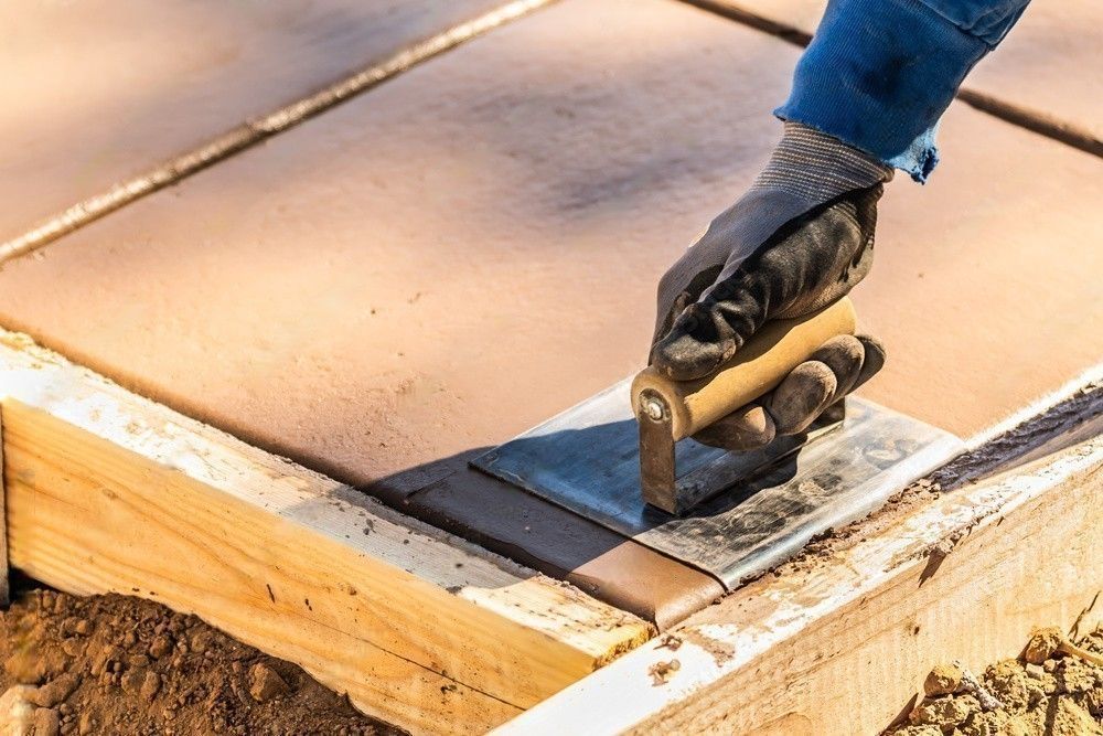 A person is using a trowel to spread concrete on a sidewalk.
