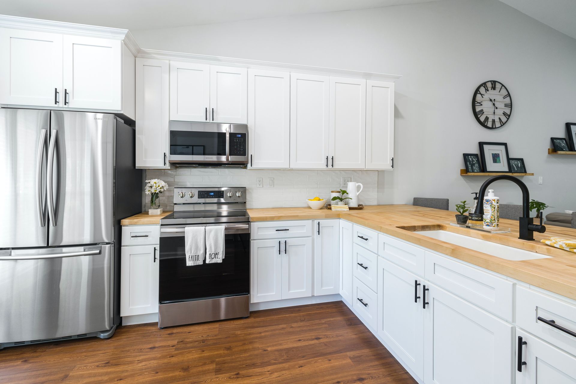 A kitchen with white cabinets , stainless steel appliances , a sink , and a clock on the wall.