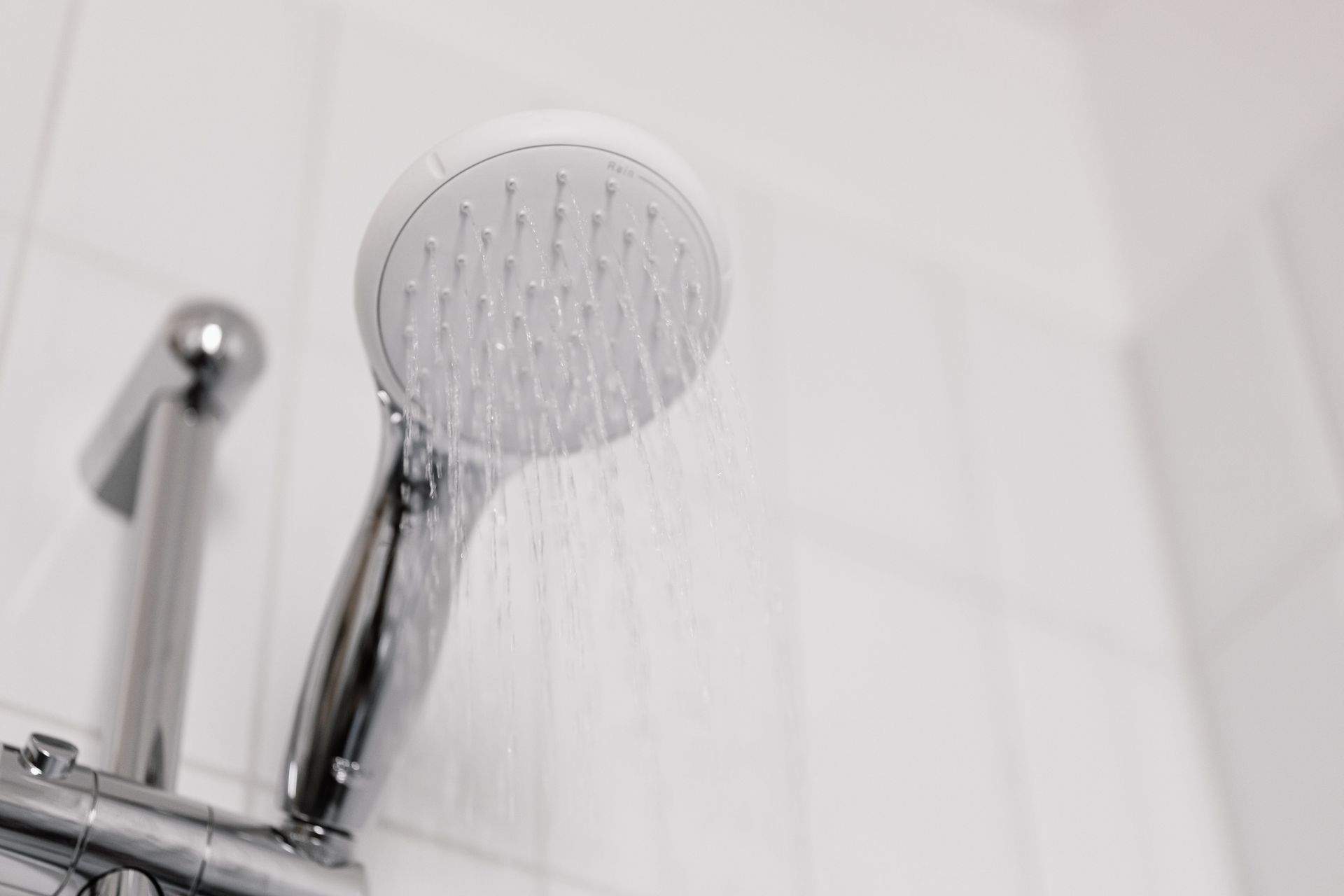 A close up of a shower head in a bathroom with water coming out of it.