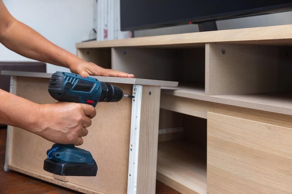 A man is using a drill to assemble a wooden entertainment center.