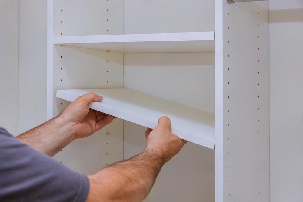 A man is taking a shelf out of a closet.