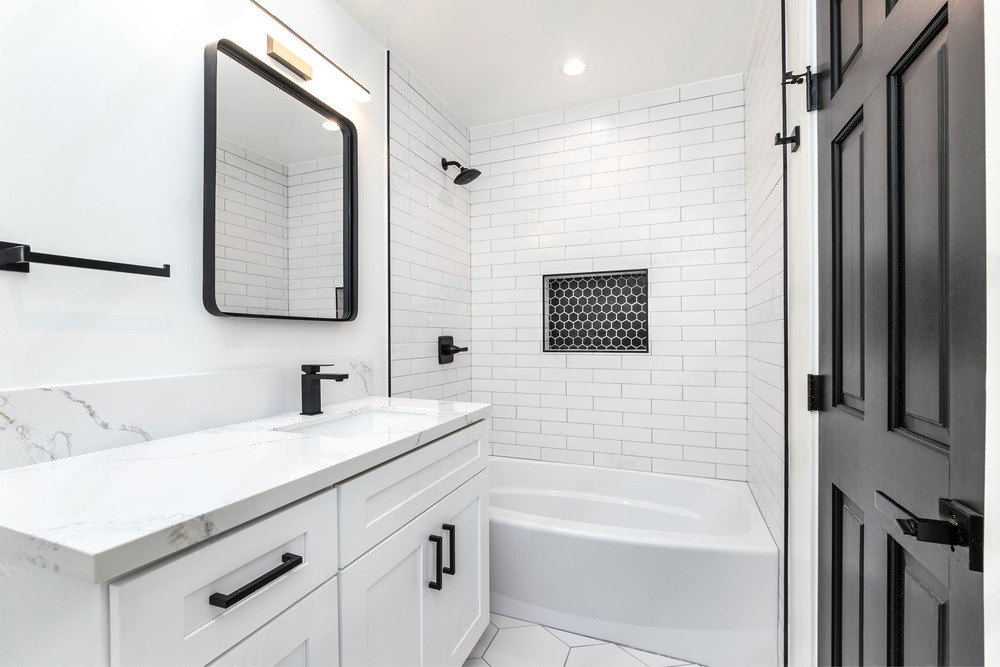 A bathroom with white tiles , a sink , a mirror and a bathtub.