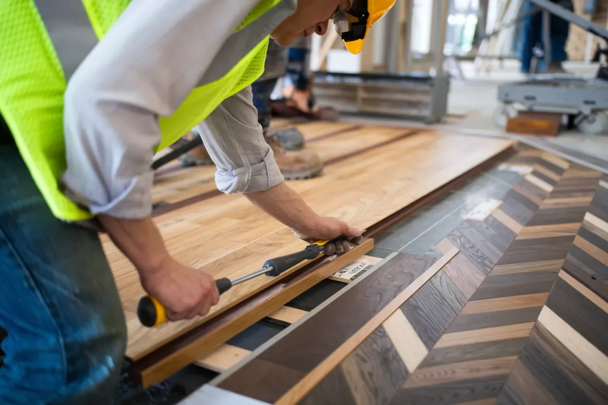 A construction worker is installing a wooden floor with a screwdriver.