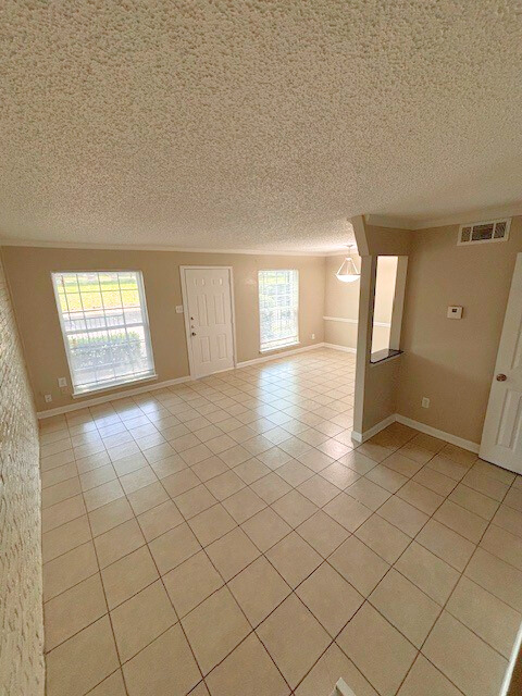 Empty living room with tile floor, windows, and white door.