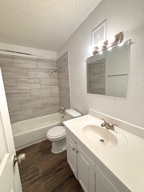 Bathroom with white vanity, toilet, and tub with tiled wall. Brown flooring.