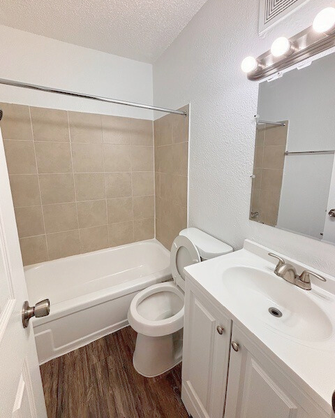 Bathroom with white walls, tan tiled tub surround, white vanity, and wood-look floor.
