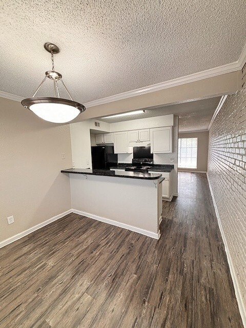 Interior of apartment with kitchen, black appliances, and wood-look flooring. White brick wall and light fixture.