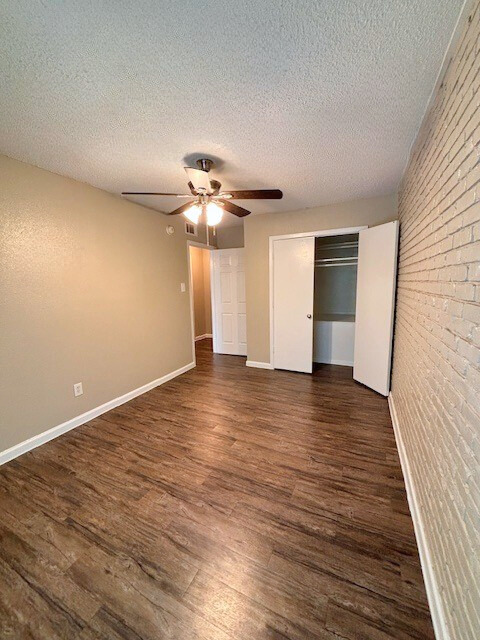 Bedroom with wood-look floor, tan walls, white closet doors, and a brick accent wall.
