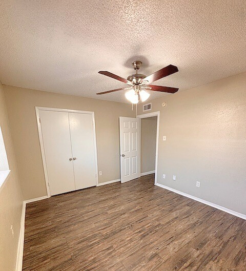 Bedroom with wood-look flooring, closet, door, ceiling fan, and beige walls.
