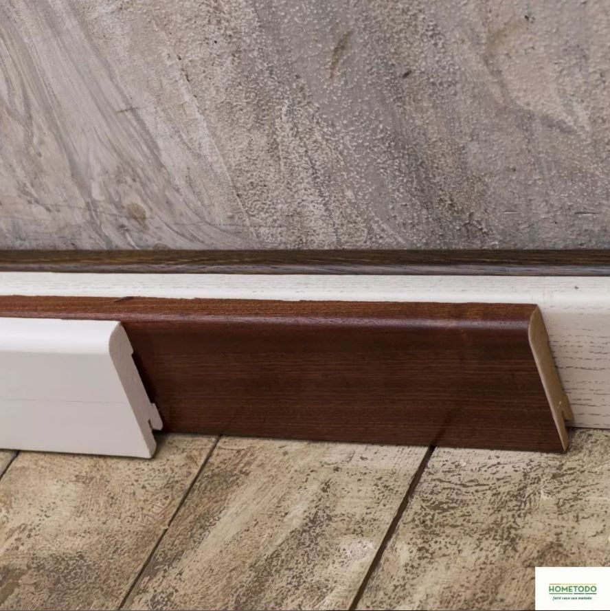 Una modanatura di legno è appoggiata su un pavimento di legno, accanto a un muro.