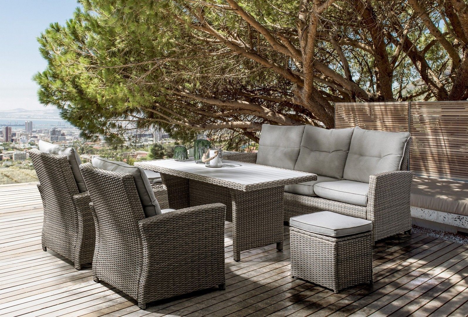 Un set da patio con divano, sedie, tavolo e pouf su una terrazza di legno.