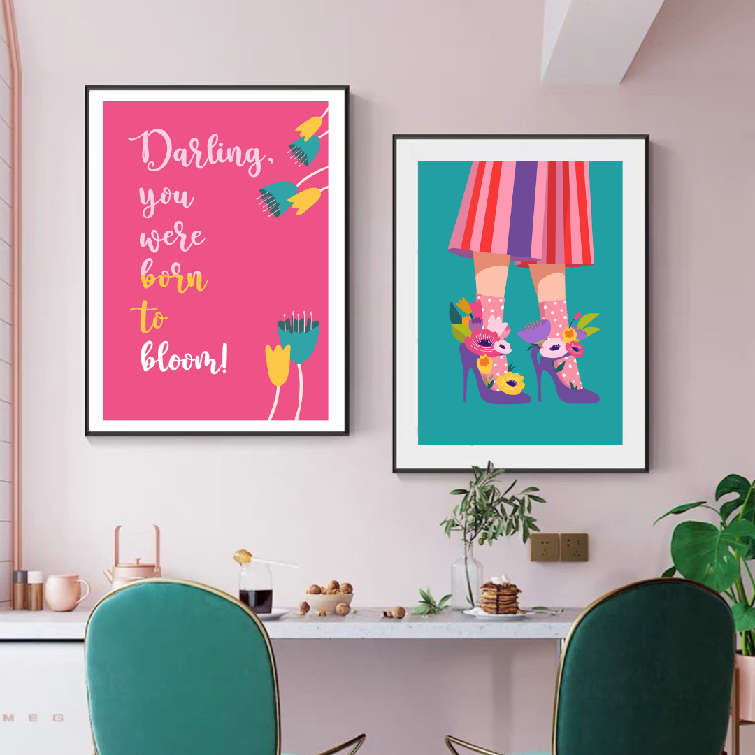 Two framed fashion posters above a desk, one pink with inspirational text and one teal with colorful striped skirt and highheels.