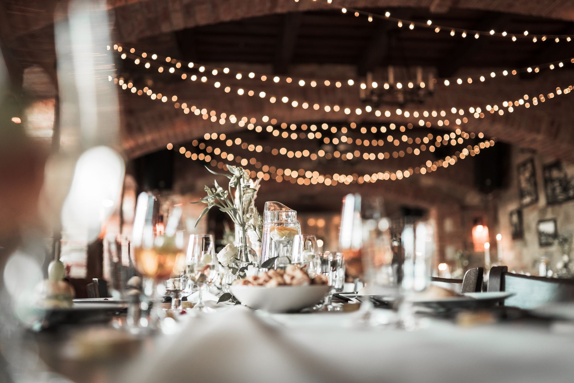 Elegant dinner table set for an event; string lights hang from the ceiling.