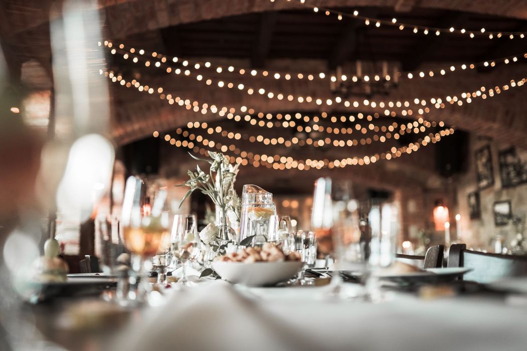 Elegant dinner table set for an event; string lights hang from the ceiling.