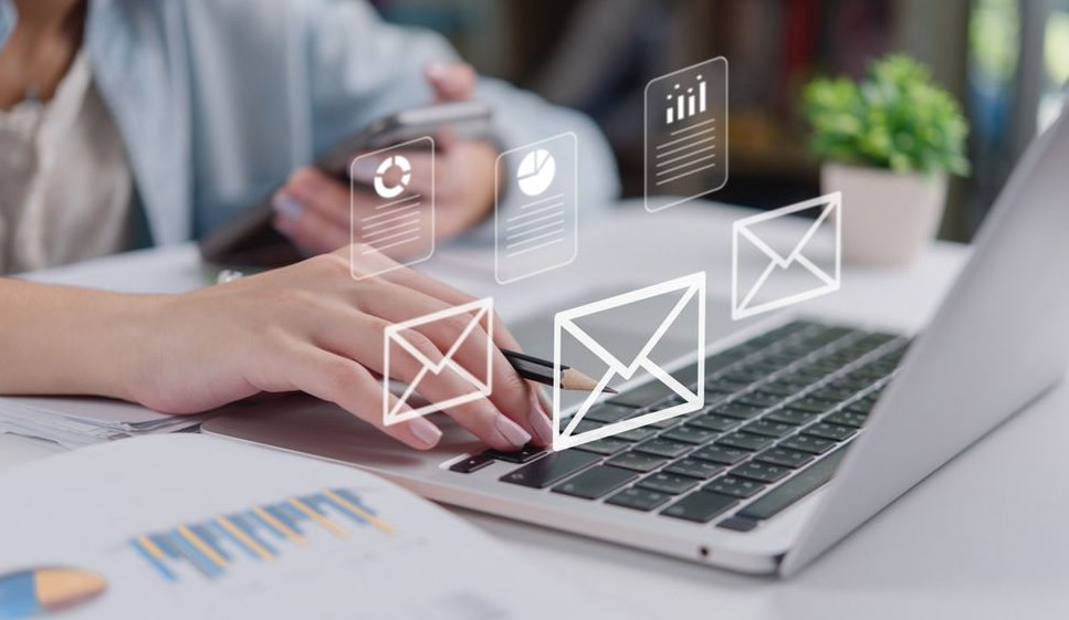A person works on a laptop at a desk with digital overlays of mail and business report icons floating above the keyboard.
