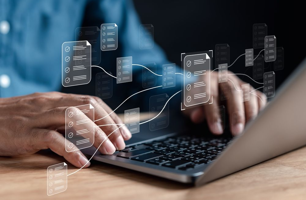 A person typing on a laptop with holographic icons of interconnected documents floating above the keyboard.