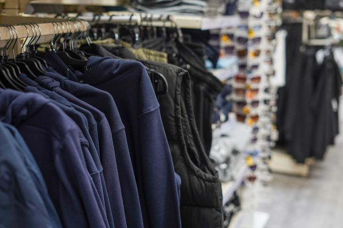 Corridoio di un negozio di abbigliamento con scaffali pieni di pantaloni e camicie scure appesi in esposizione