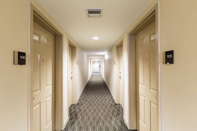 Hotel hallway with beige doors, patterned carpet, and bright light at the end.