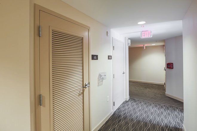 Hallway with a ventilation door, exit sign, and carpet.