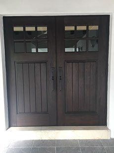 Dark wood double doors with glass panel tops and vertical paneling, in a white doorway.
