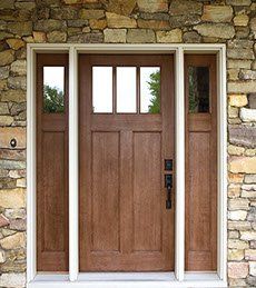 Brown front door with sidelights, set in stone wall with white trim.