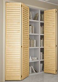 Wooden louvered bi-fold closet doors open to reveal a white built-in bookshelf filled with books.