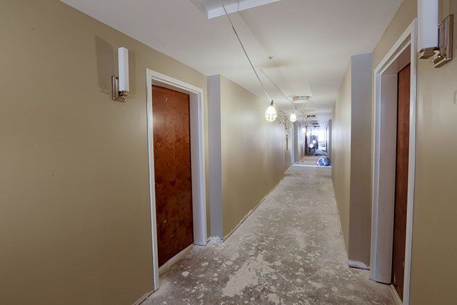 Hallway with tan walls, brown doors, and exposed flooring covered with debris.