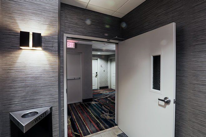 Hallway with a white door, a wall light, and patterned wallpaper. View into another hallway with doors.