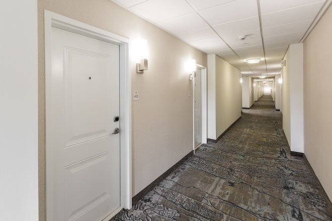 Hallway with beige walls, patterned carpet, and several white doors with lights.