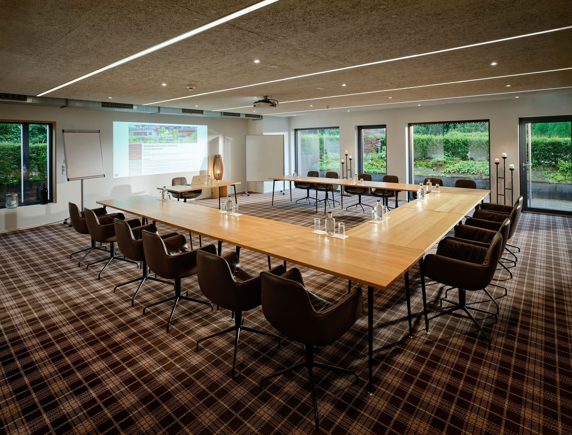 Moderner Konferenzraum mit langem Tisch, schwarzen Stühlen, Holzlattenwand, Betonwänden und Tafel.