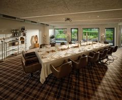 Elegantes Esszimmer mit langem Esstisch, braunen Stühlen und großen Fenstern mit Blick ins Grüne