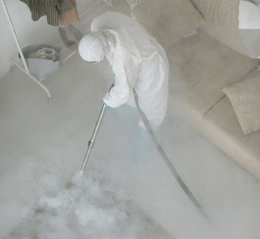 A person in a protective suit is cleaning the floor with a vacuum cleaner.