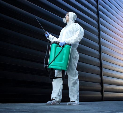 A man in a protective suit is holding a green sprayer