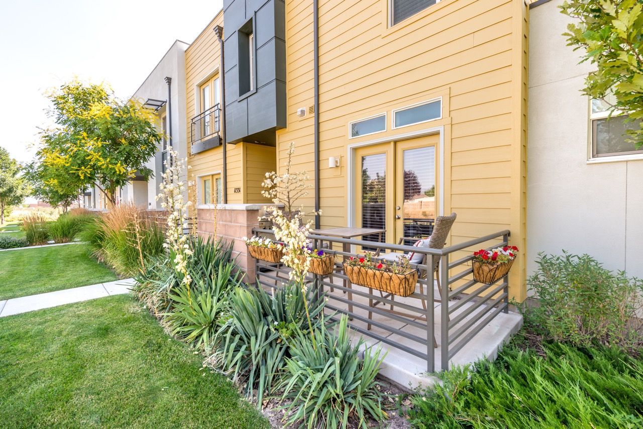 Exterior of a modern apartment building with a small porch, metal railing, and flower planters along the entrance.