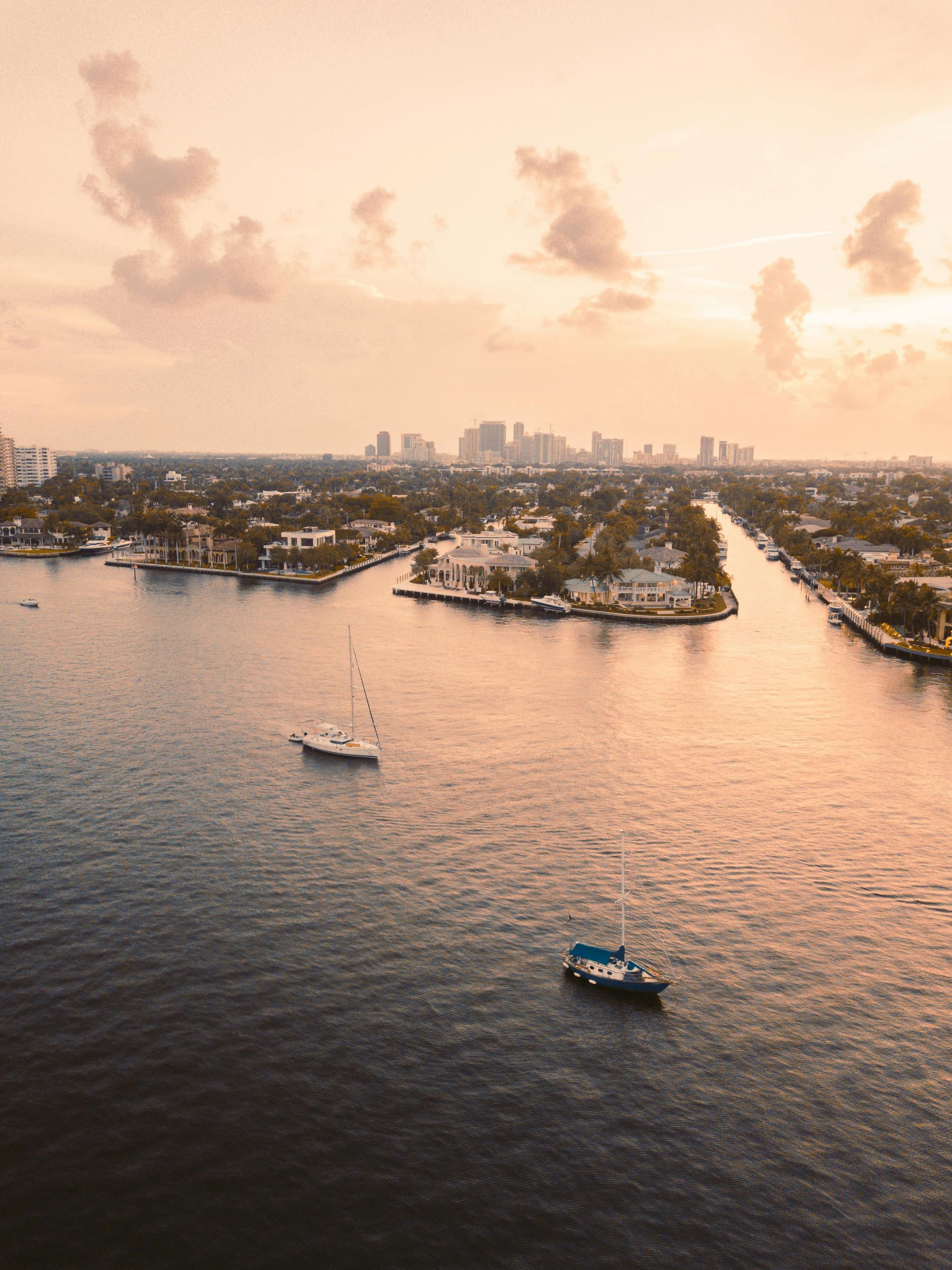 Aerial view of a waterway with boats, luxurious houses, and a city skyline at sunset.