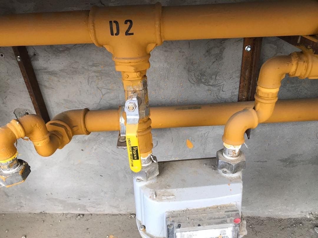 Tuberías de gas amarillas con válvula y medidor en una pared de hormigón, etiquetadas