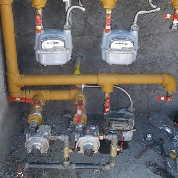 Medidores y reguladores de gas con tuberías y válvulas amarillas, instalados en una pared de hormigón.