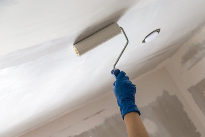 A hand of worker in a blue glove is painting the ceiling with primer.