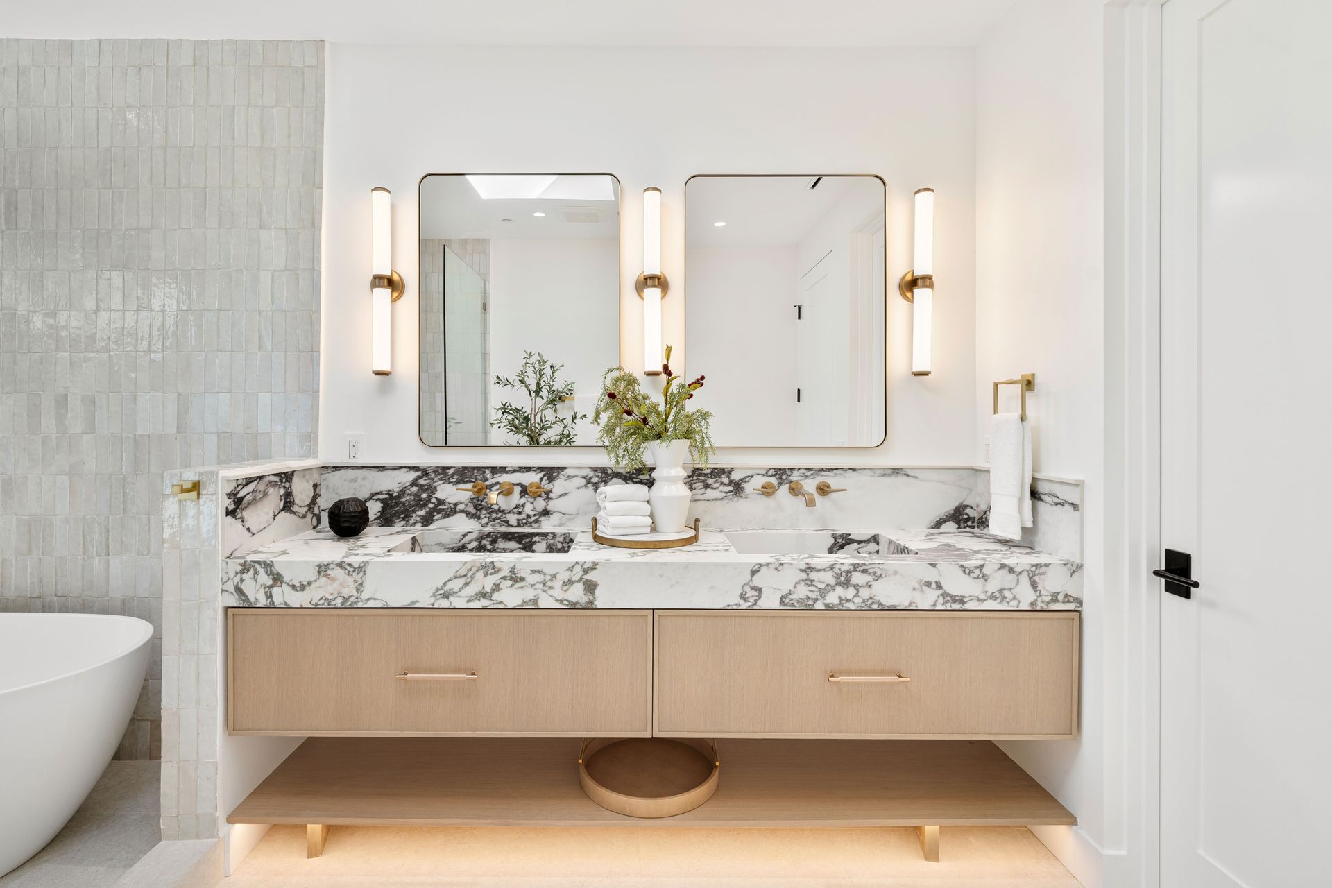 A bathroom with two sinks , a tub , and a mirror.