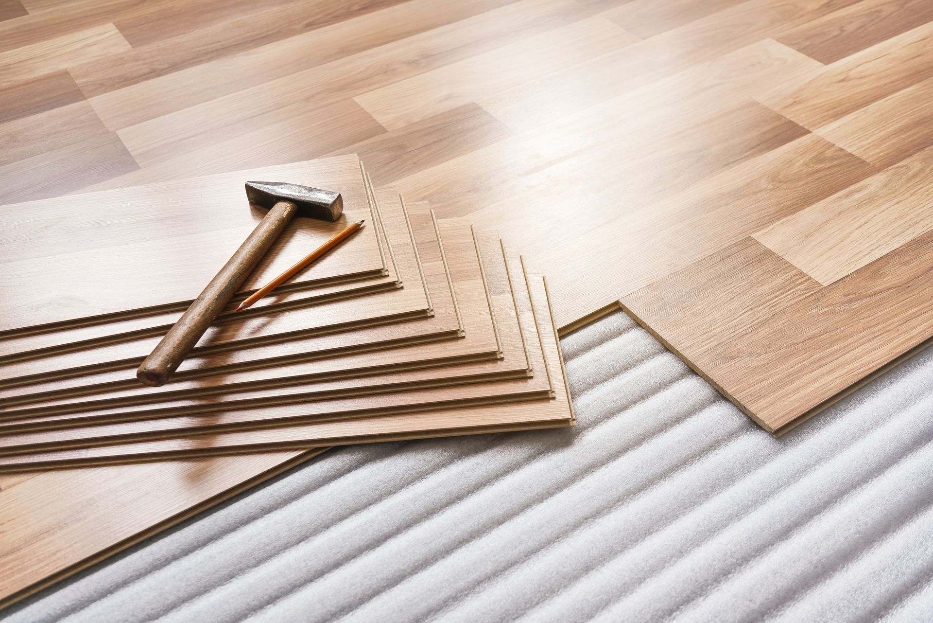 A hammer is sitting on top of a stack of wooden flooring.