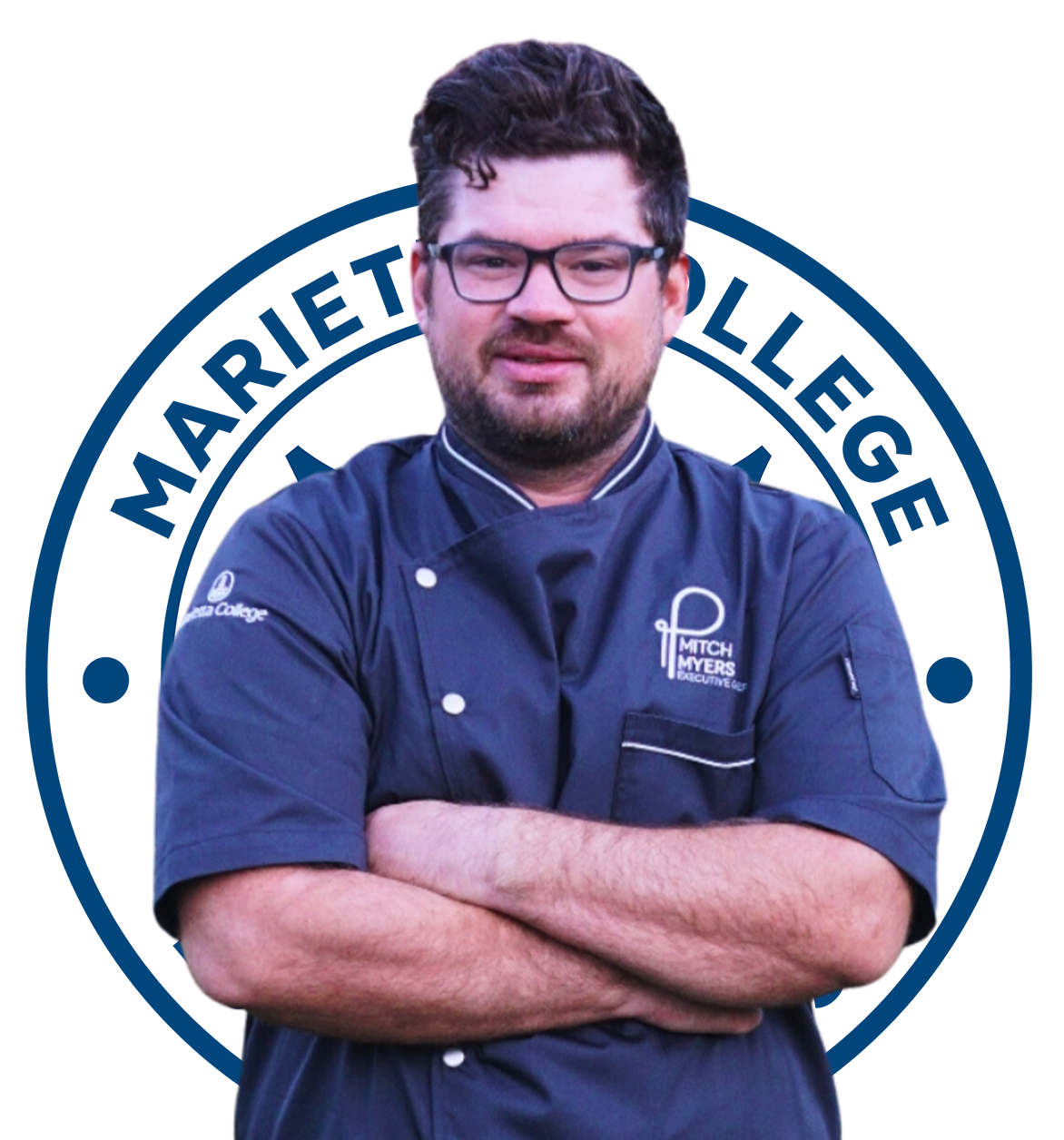 Man in chef's uniform with crossed arms, wearing glasses. The emblem of a culinary institute is in the background.
