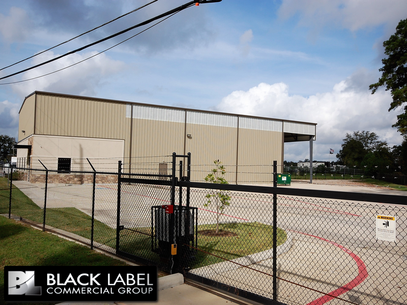 A large building with a chain link fence and a black label commercial group logo