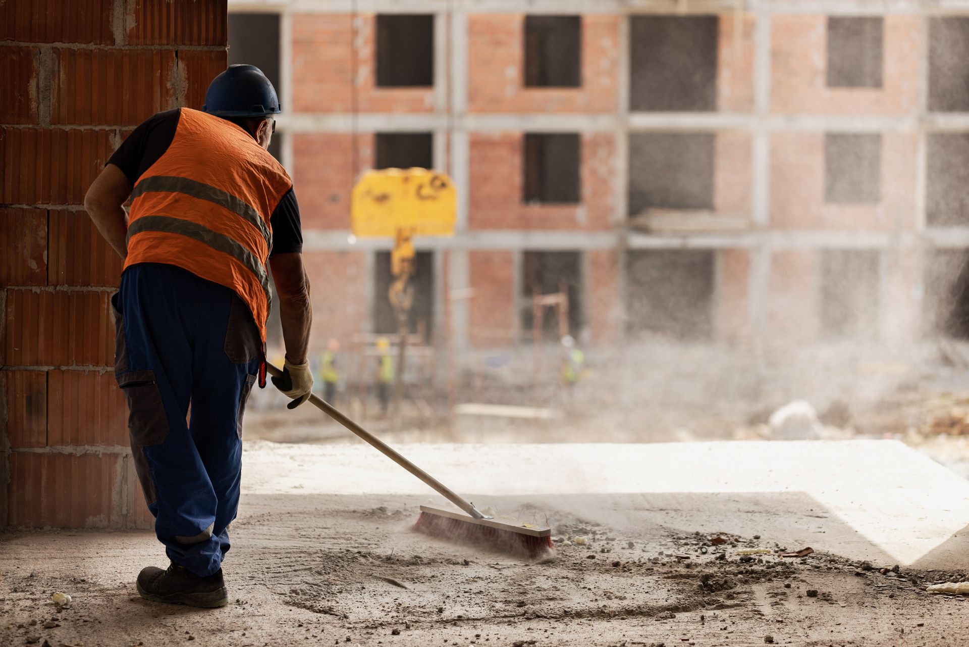 A man is mopping the floor of a warehouse next to a caution sign.