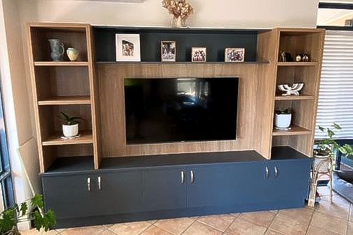 A living room with a flat screen tv and shelves.