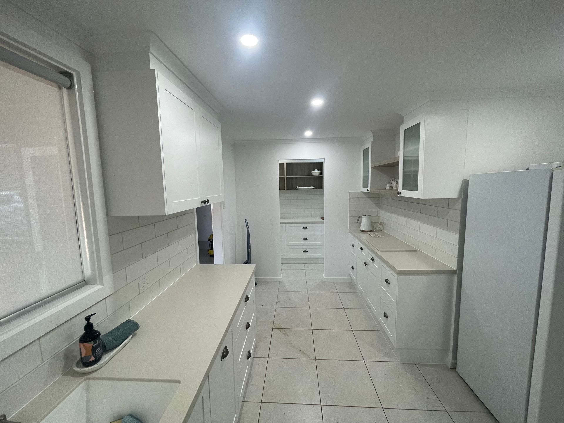 A kitchen with white cabinets , a sink , a refrigerator and a window.