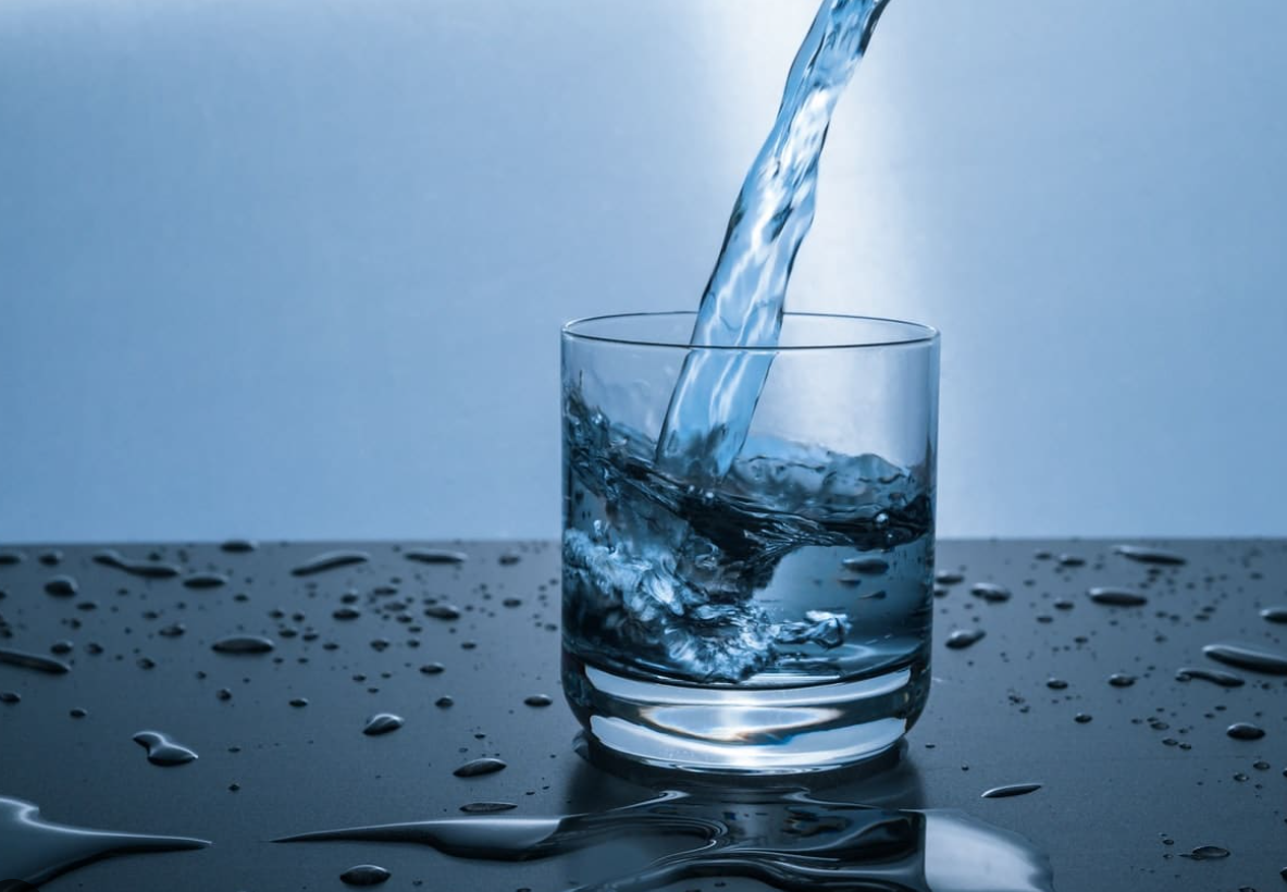 Water being poured into a clear glass, with water droplets on the surrounding reflective surface. — Bennett's Servicing and Plumbing In South Nowra, NSW
