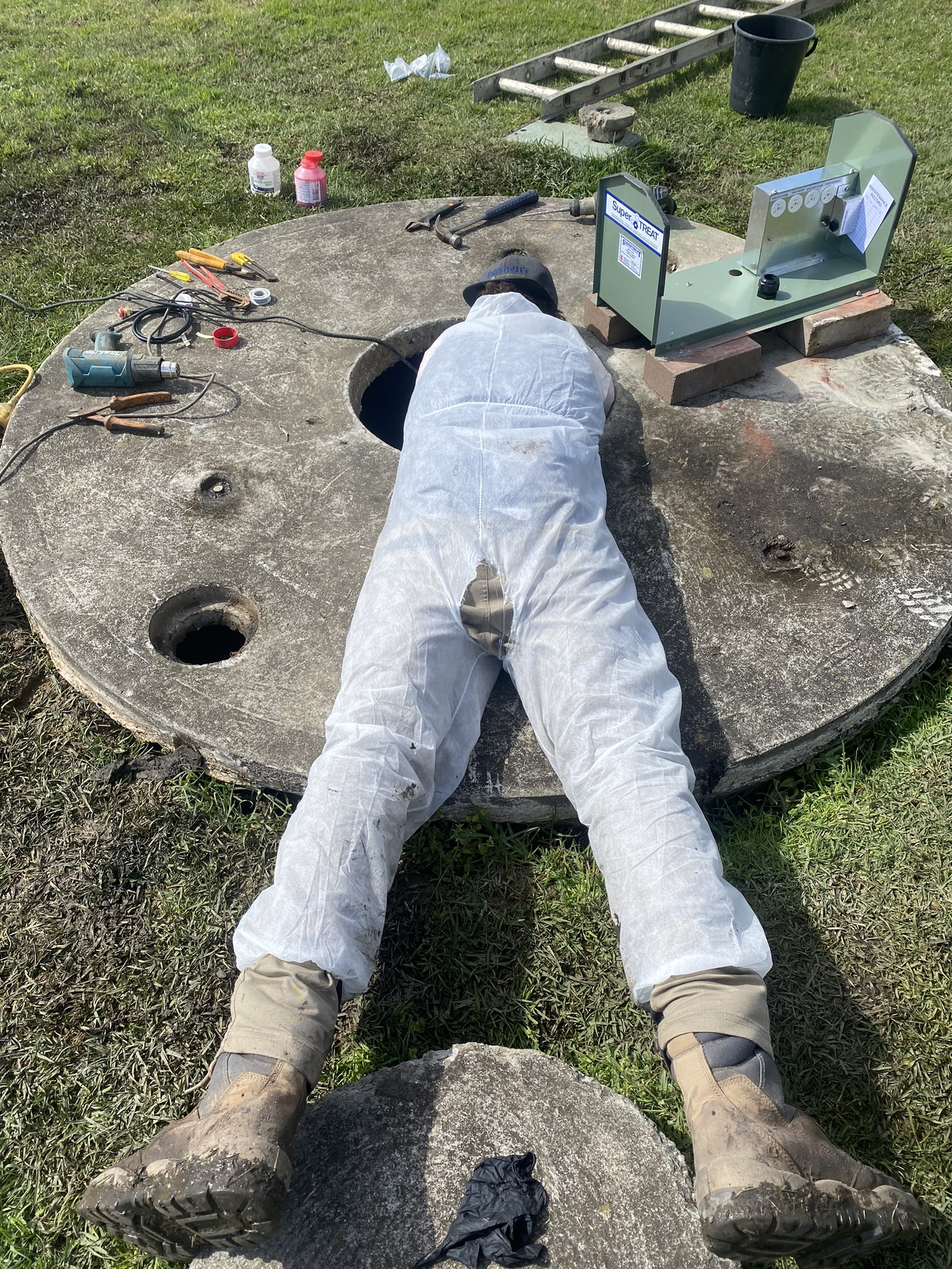 Person in protective suit working on a concrete structure with tools nearby. — Bennett's Servicing and Plumbing In South Nowra, NSW