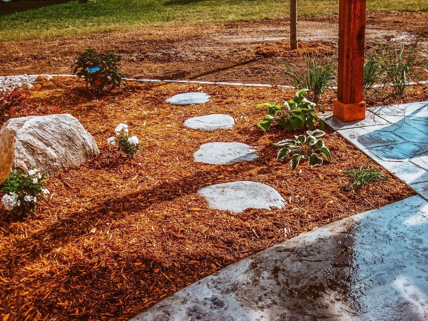 Stepping stones through wood chip mulch in a garden, next to a patio.
