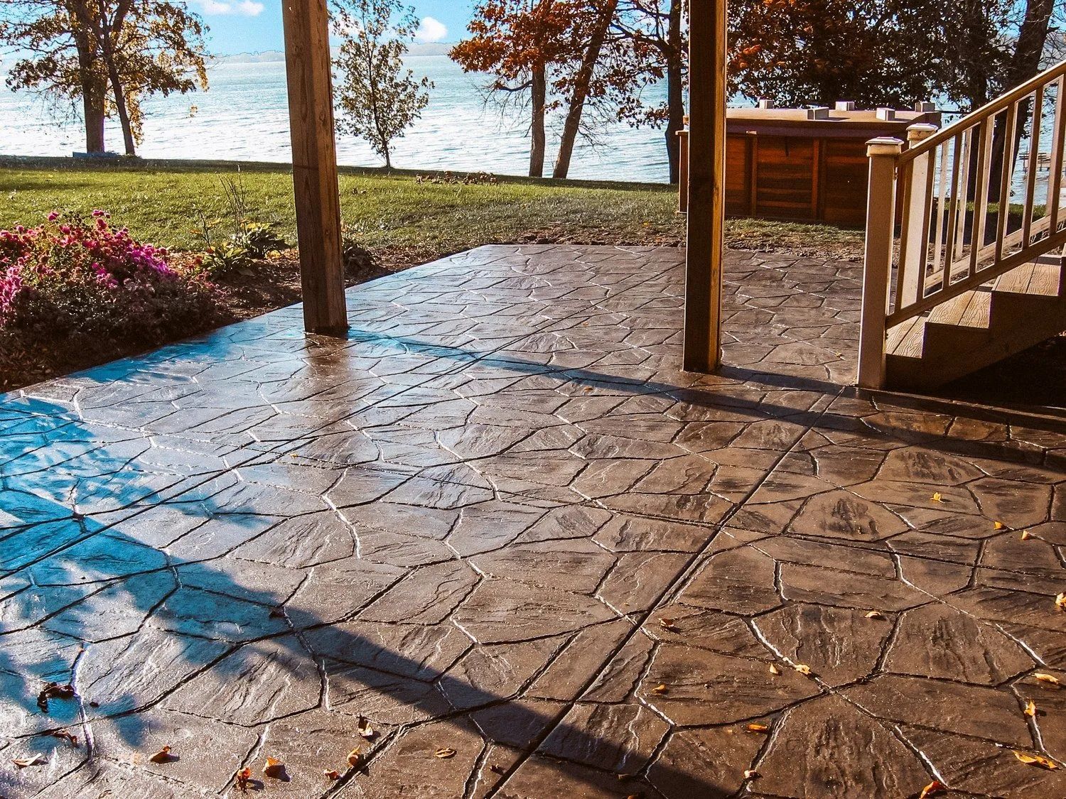 Concrete patio with a flagstone pattern, overlooking a lake and grassy lawn.